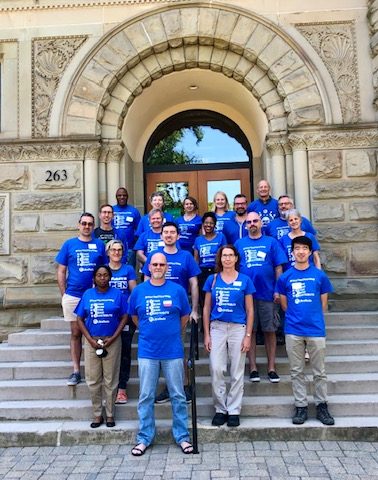 collection of a dozen people wearing libretexts blue shirts on the stairs of a stone archway doorway